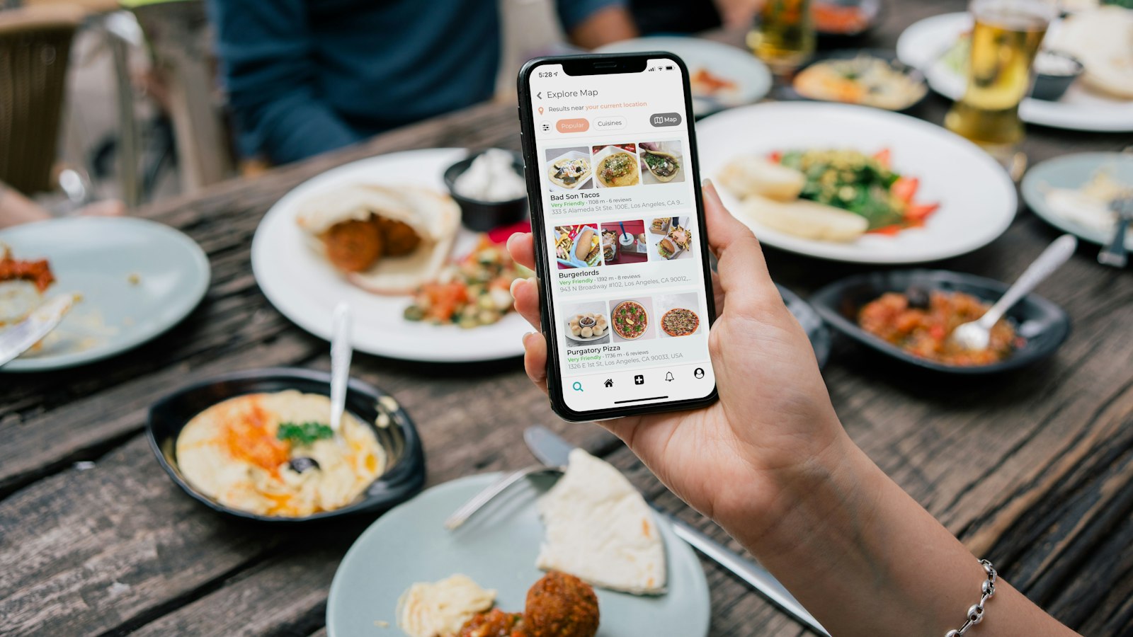 Une main tient un smartphone affichant un menu au-dessus d'une table de restaurant garnie de plats